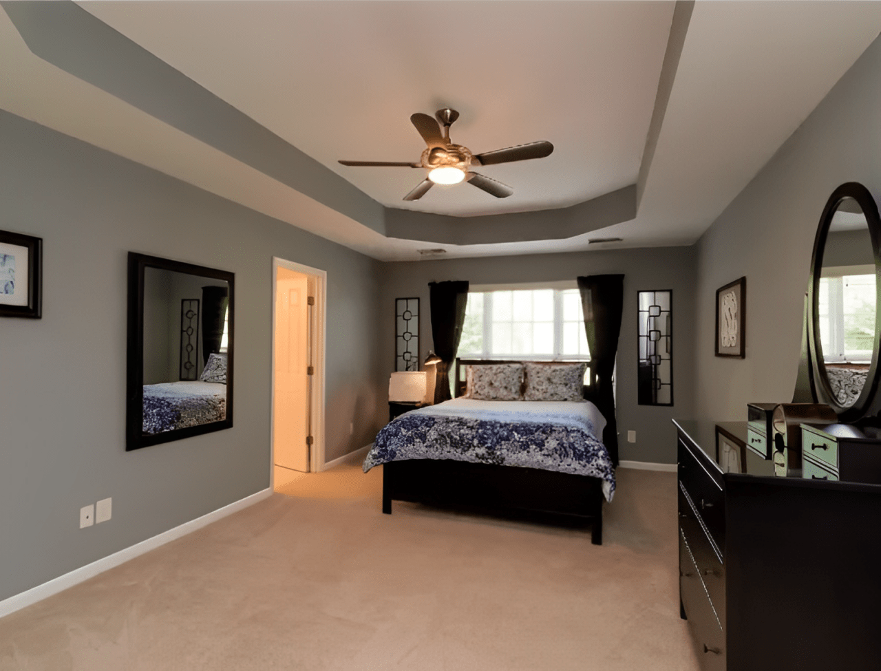 Cozy bedroom featuring a queen-sized bed with blue bedding, two mirrors, a ceiling fan, and an adjoining door leading outside.