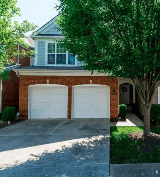 Brick house exterior featuring a two-car garage, large windows, and surrounding greenery, emphasizing a well-maintained suburban setting.