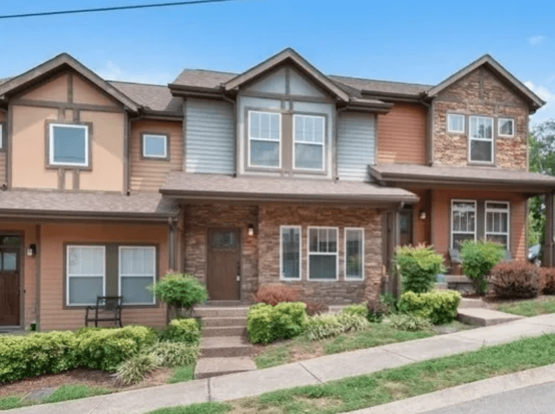 Modern townhouses with a mix of stone and siding, showcasing landscaped front yards and a clear blue sky, suitable for a real estate listing.