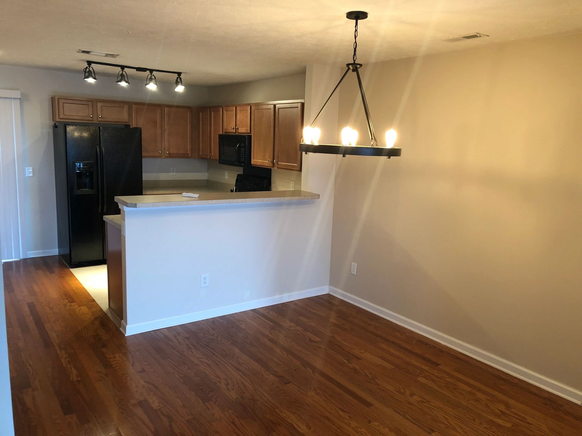 Modern kitchen and dining area with hardwood floors, featuring dark appliances, wooden cabinetry, and a stylish chandelier for illumination.