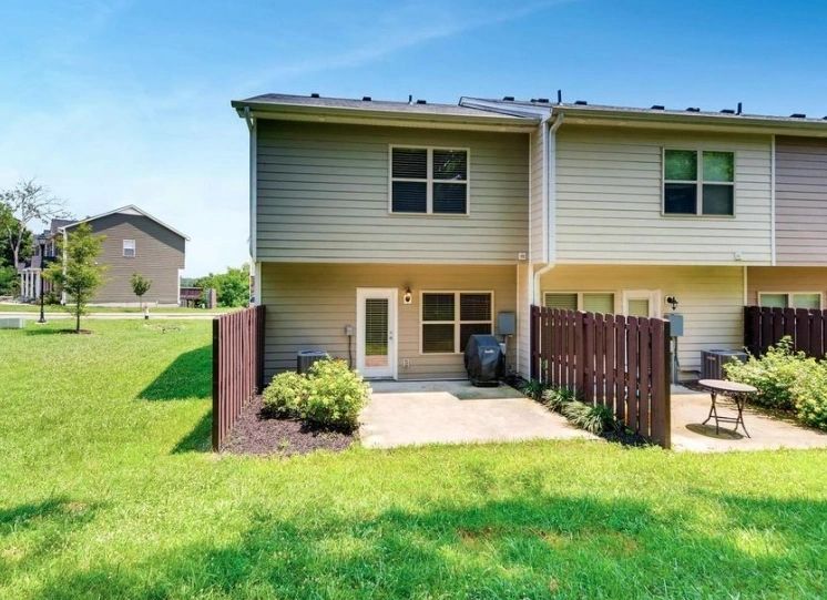 Two-story townhouse exterior featuring a fenced patio area, lush green lawn, and outdoor seating. Ideal for showcasing property layout and outdoor space.