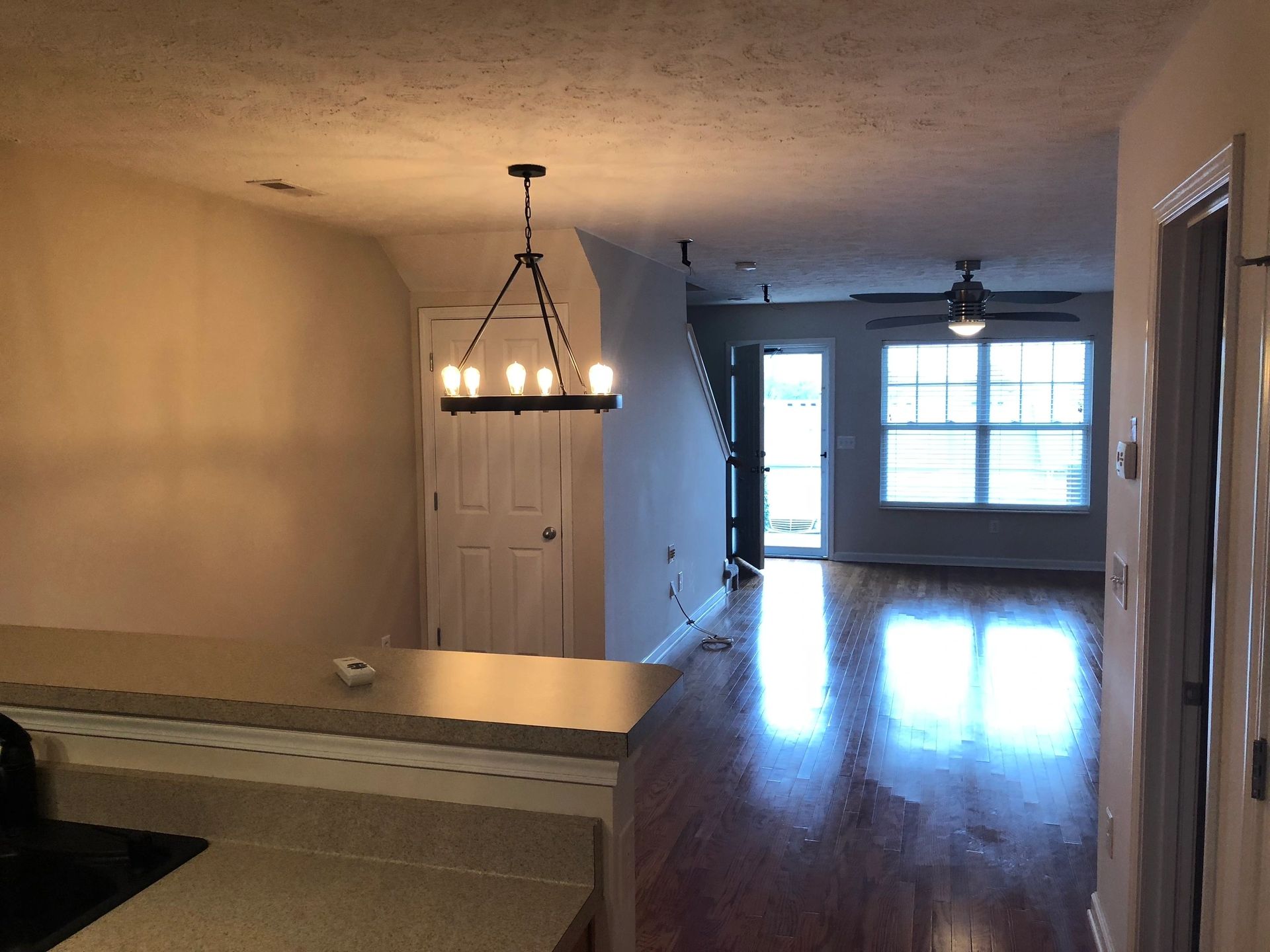 Light-filled open-concept living area showcasing hardwood floors, a contemporary chandelier, and a door leading to a patio. Ideal for modern living.