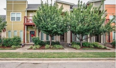 Colorful apartment complex featuring well-maintained landscaping and two prominent trees flanking the entrance, highlighting a welcoming atmosphere.